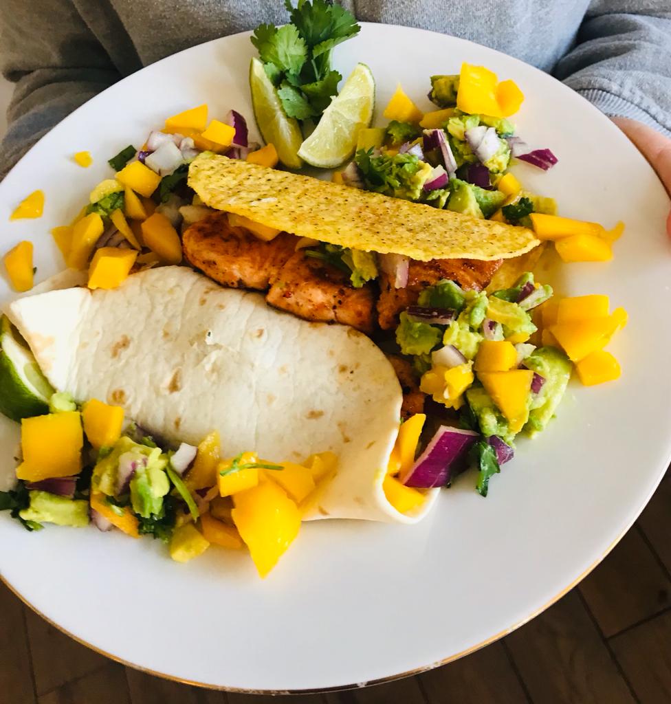 Two chicken and mango tacos on a plate, garnished with avocado, onion and lime.