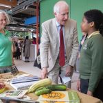 Government Minister Daniel Zeichner talks to two children in front of a table of vegetables they've grown.