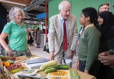 Government Minister Daniel Zeichner talks to two children in front of a table of vegetables they've grown.