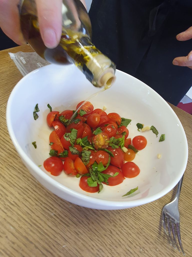 A hand pours olive oil over tomatoes